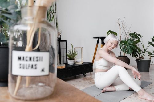 Smiling woman with short white hair practicing yoga indoors surrounded by plants.